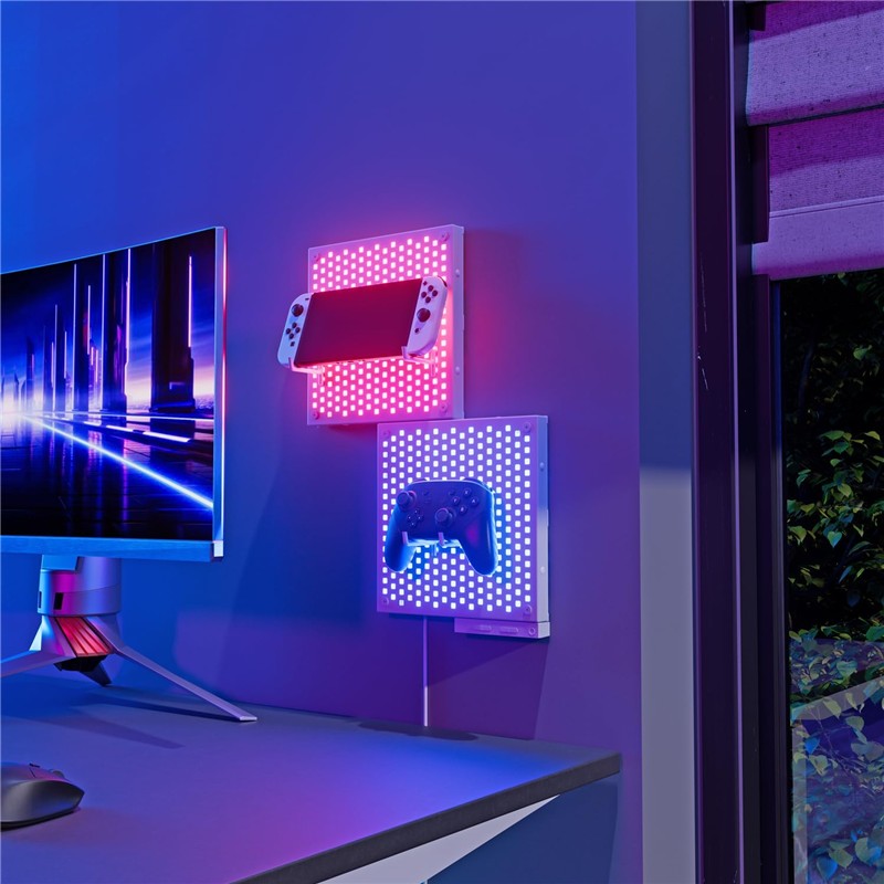 Dos paneles de luz Nanoleaf Blocks en la pared junto a un monitor, sosteniendo una consola portátil y un control